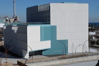 The white and turquoise EEBE Building I, seen from above, with the sea in the background